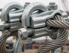 Heavy duty galvanized U-bolt rope clamps with grooved saddle plates securing thick steel cable for industrial rigging application