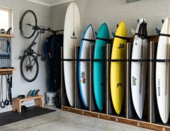 Wooden rack displaying three surfboards horizontally inside a clean garage.