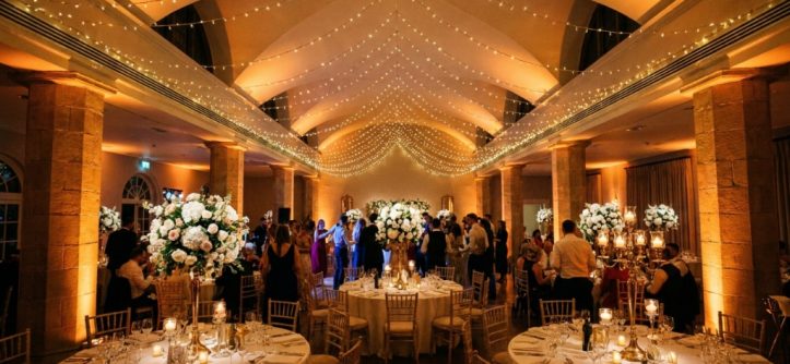 Warm uplighting illuminates stone columns in an elegant wedding reception ballroom.