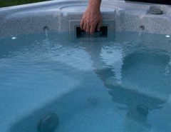 Technician cleaning a clogged spa filter cartridge with a garden hose outdoors
