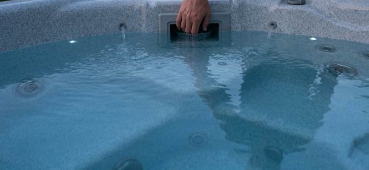 Technician cleaning a clogged spa filter cartridge with a garden hose outdoors