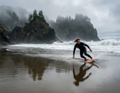 Skimboarder riding a shallow water reflection on a foggy Pacific Northwest shorebreak beach.