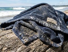 Wet surf poncho draped over driftwood covered in sand.