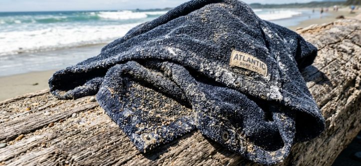 Wet surf poncho draped over driftwood covered in sand.