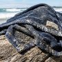 Wet surf poncho draped over driftwood covered in sand.